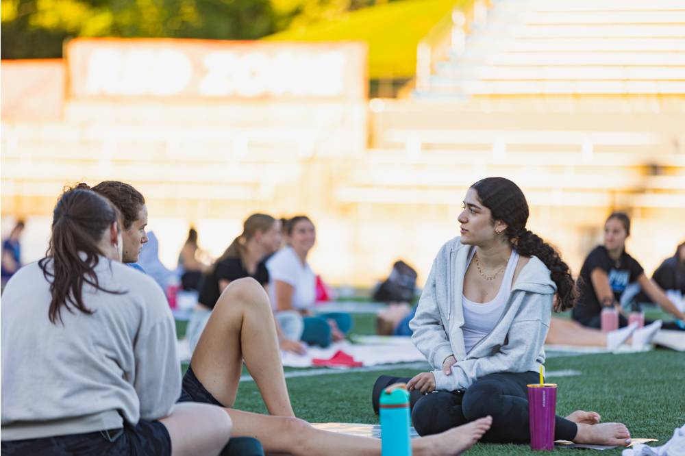 Students sitting on the Football Field during a yoga session at sunset